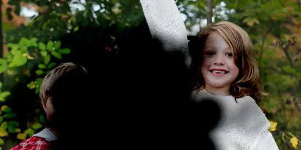 Smiling child with partial vision loss raising arm, outdoors with blurred dark area simulating eye condition