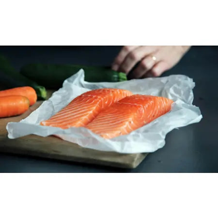 Raw salmon fillets on parchment paper with fresh carrots and zucchini on a wooden board