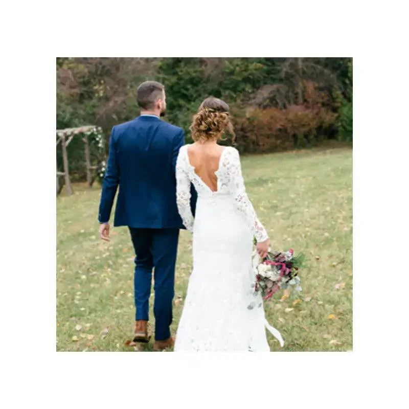 Bride in lace wedding dress holding bouquet walking with groom in blue suit outdoors