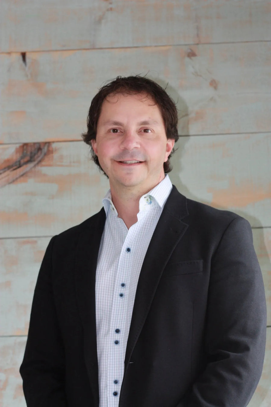 Smiling man in a suit jacket and dress shirt against a rustic wooden background